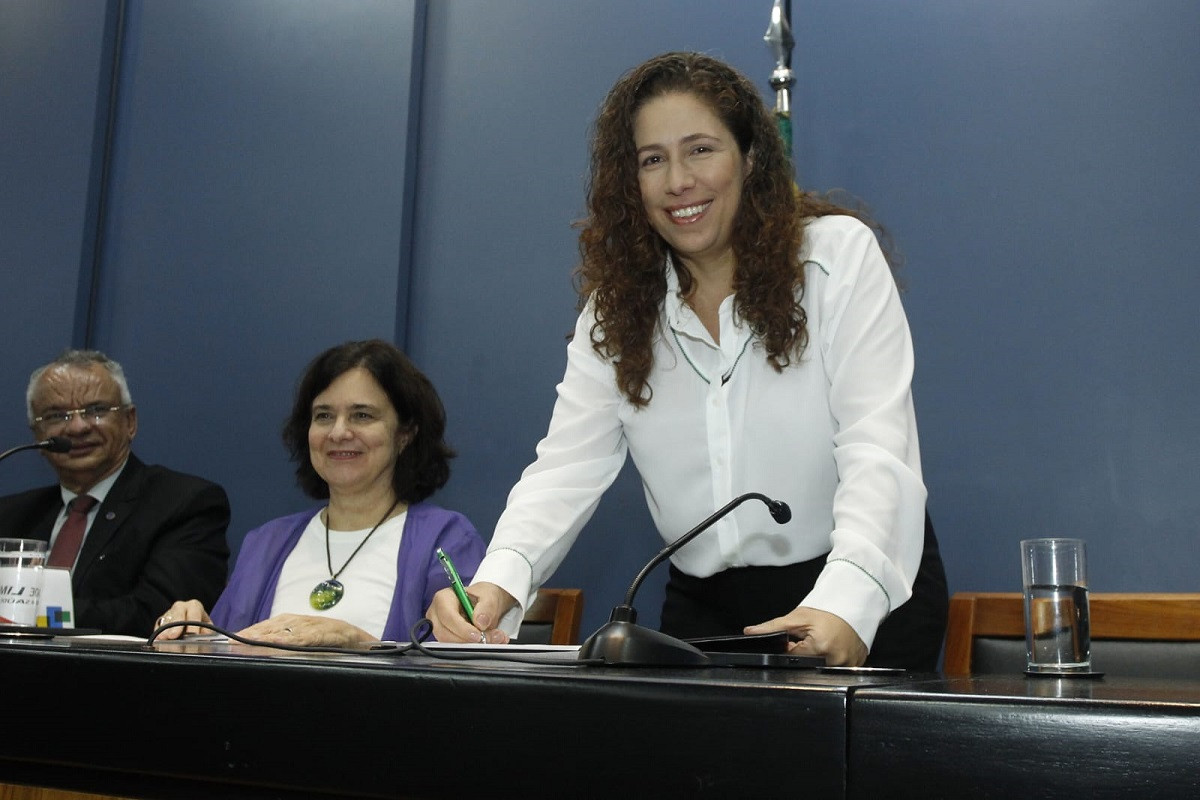 Ministra Esther Dweck assina documento e sorri para câmera